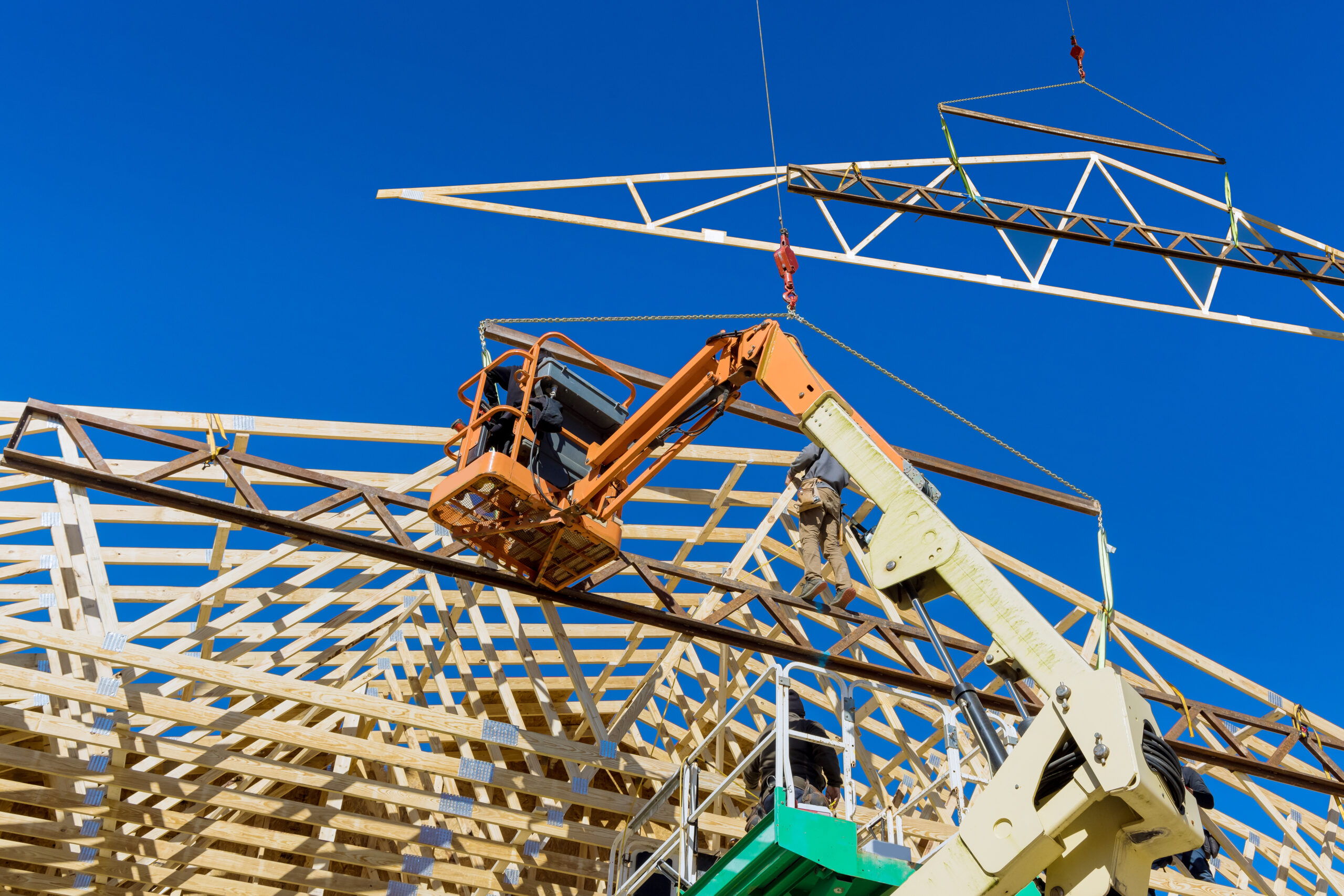Construction worker using air hammer nailing beams of wooden frame roof on rafters in his domestic building with wooden framework beams
